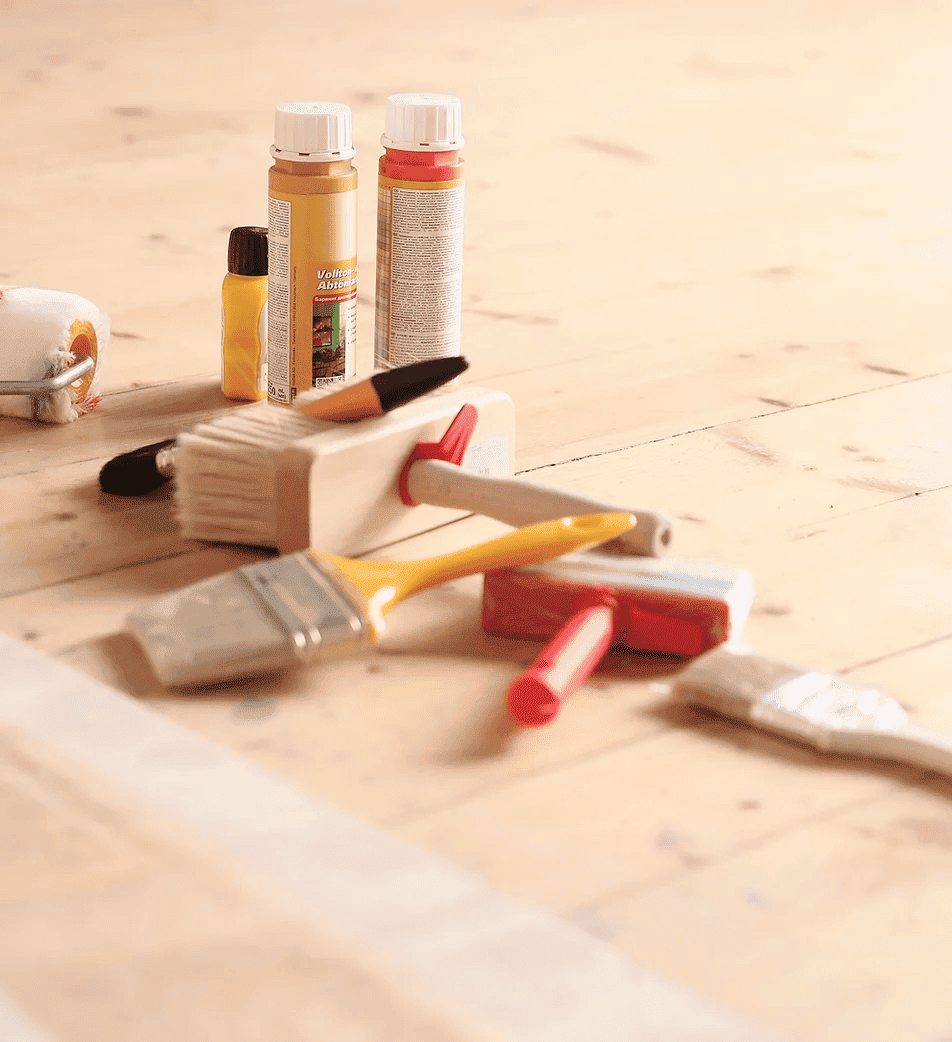 Brochas y botes de pintura sobre parquet antes de pintar.