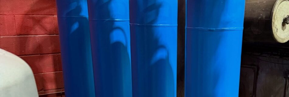 Bombonas metálicas de butano recién pintadas en azul durante el proceso de aplicación de pintura industrial.