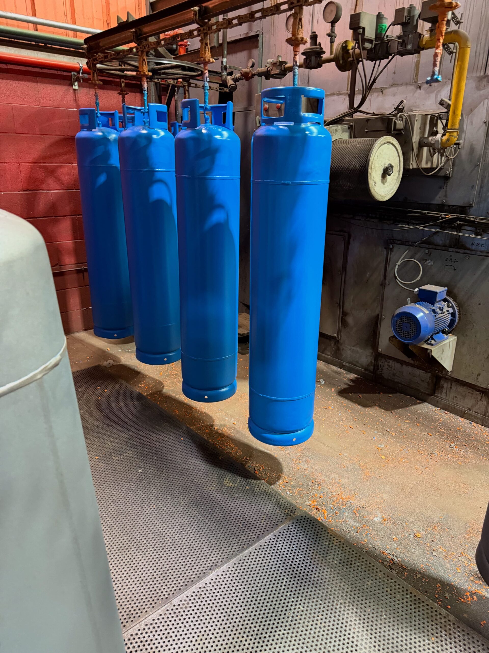 Bombonas metálicas de butano recién pintadas en azul durante el proceso de aplicación de pintura industrial.